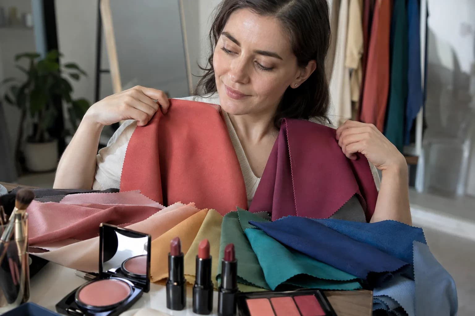 Warm, cool, muted, and bright fabric drapes arranged beside rose, coral, and berry makeup shades for seasonal color analysis